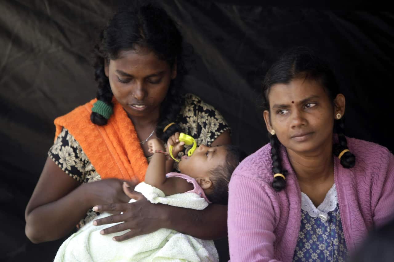 Sri Lankan women with a baby rest inside a tent.