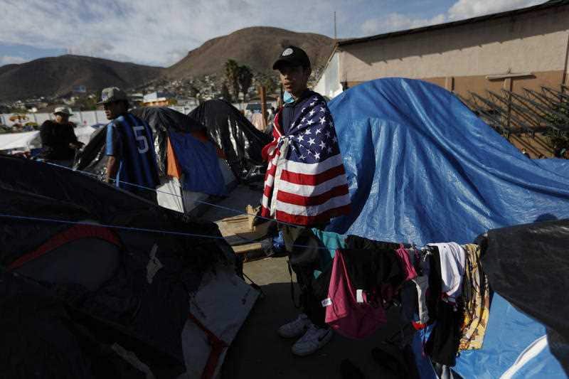 Daniel Castilla, 19, from Honduras, wears a US flag as he looks out over migrant tents at a former concert venue serving as a shelter, in Tijuana, Mexico.