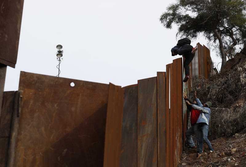 A Honduran migrant is boosted up by his father and a friend as they jump the US border wall.A Honduran migrant is boosted up by his father and a friend as they jump the US border . The president is demanding backing for an extended border wall.