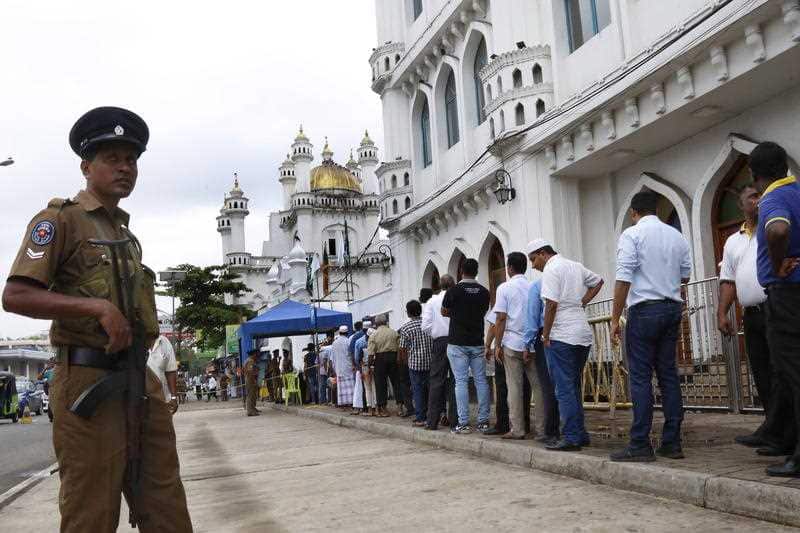 Sri Lankan security forces stand guard while Muslim people queue up for security checking before enter the Friday prayers.