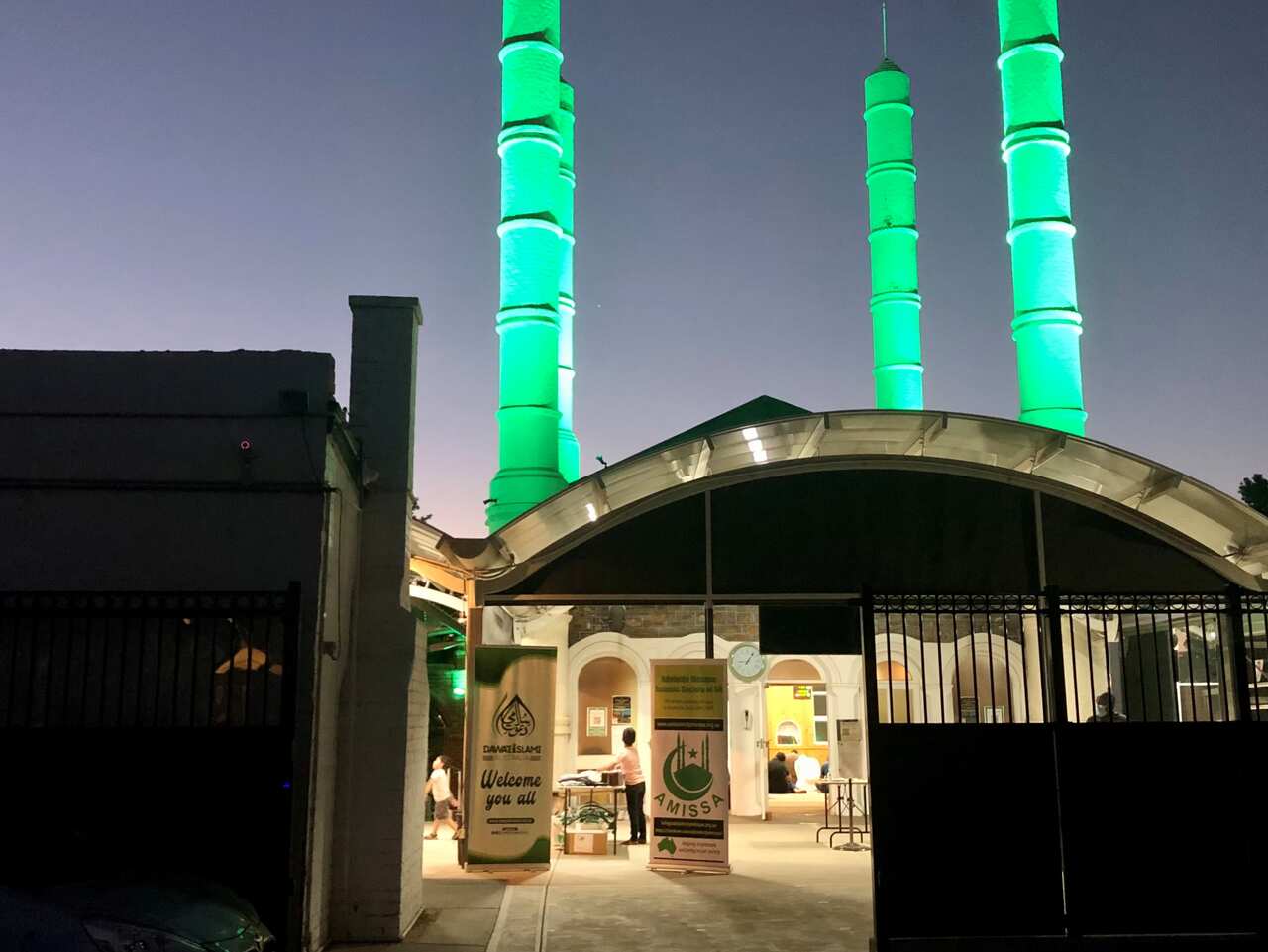 The exterior of the Adelaide Mosque at dusk, lit up with green lights.