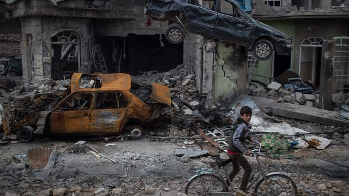 A boy rides his bike past destroyed cars and houses in a neighborhood recently liberated by Iraqi security forces.