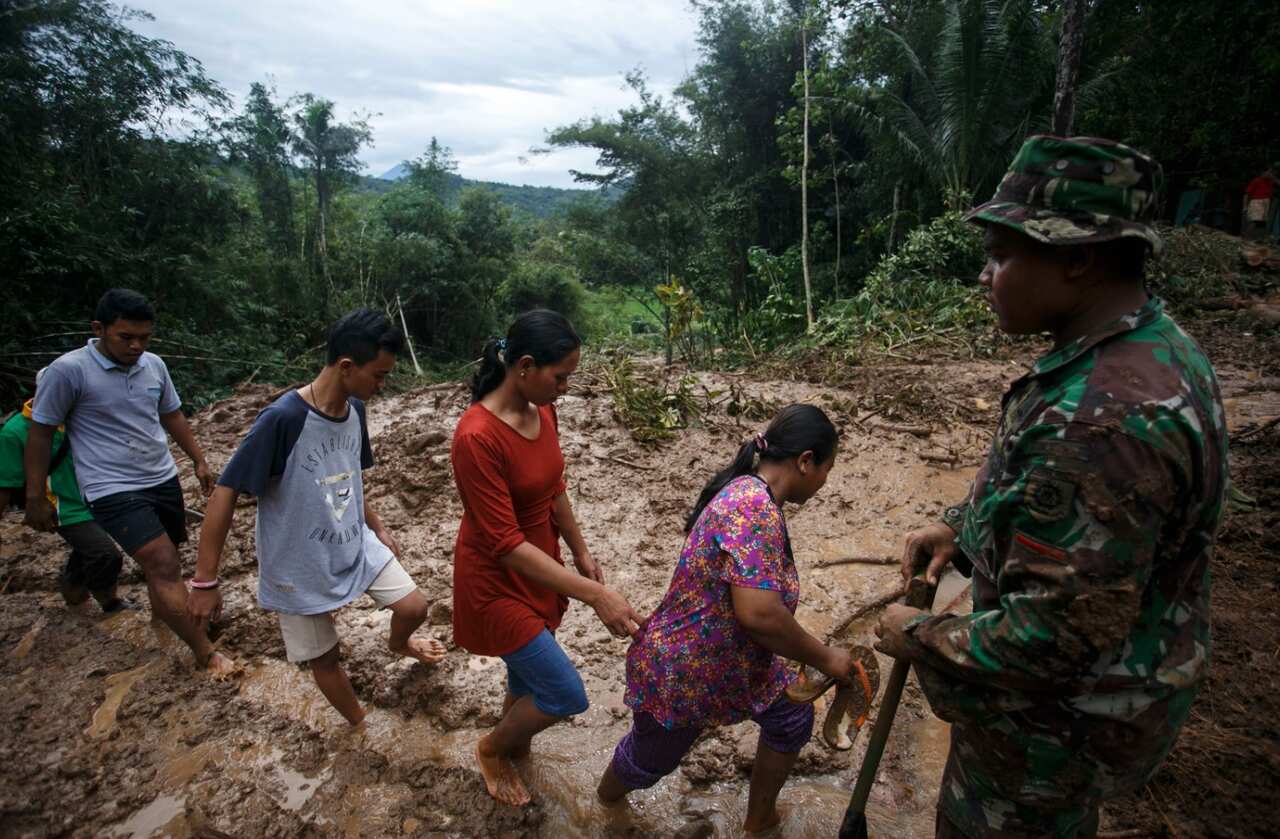 Residents walk pass as an Indonesian soldier stand guard at a landslide area in Purworejo, Indonesia, 19 June 2016. 