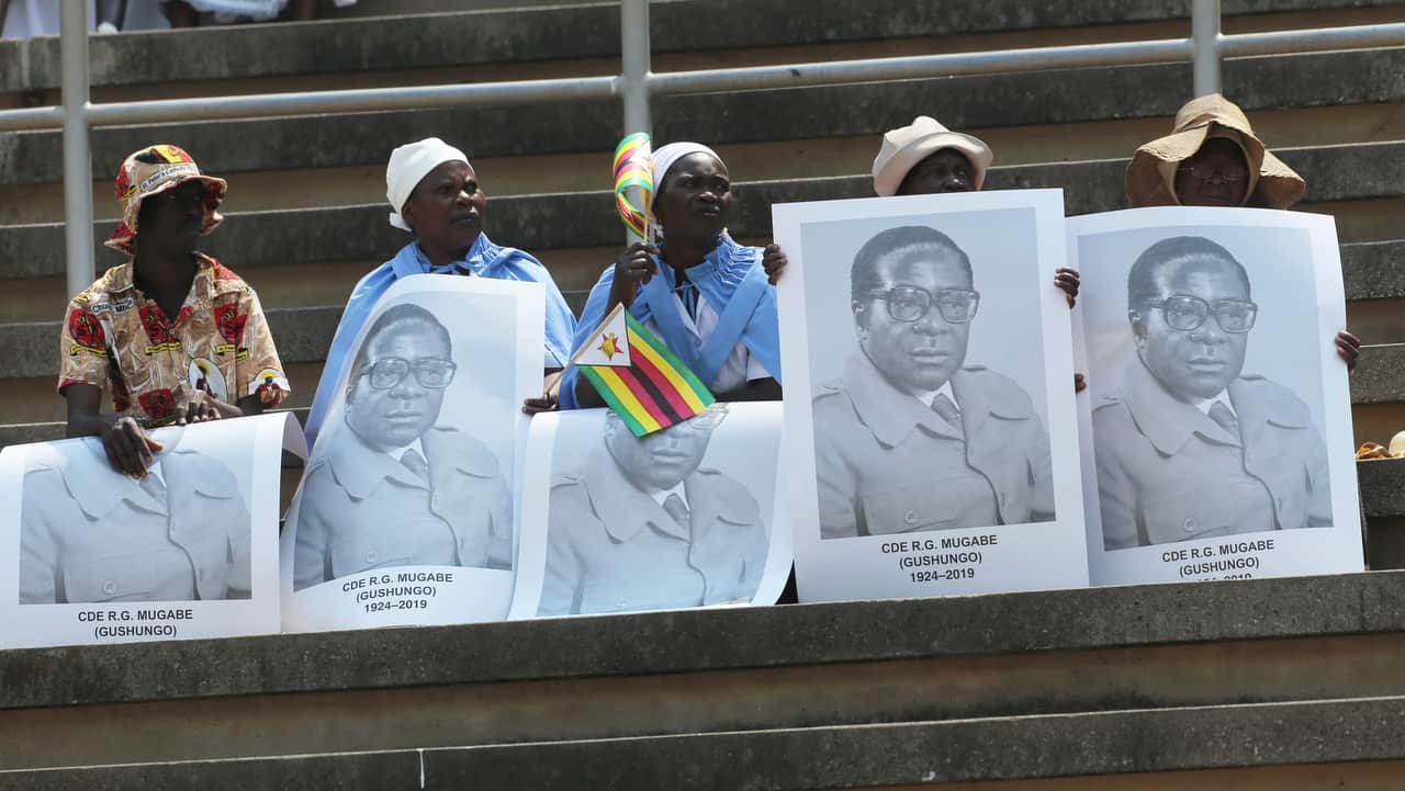 Supporters of Robert Mugabe carry his portrait as his remains arrive at the National Sports stadium.