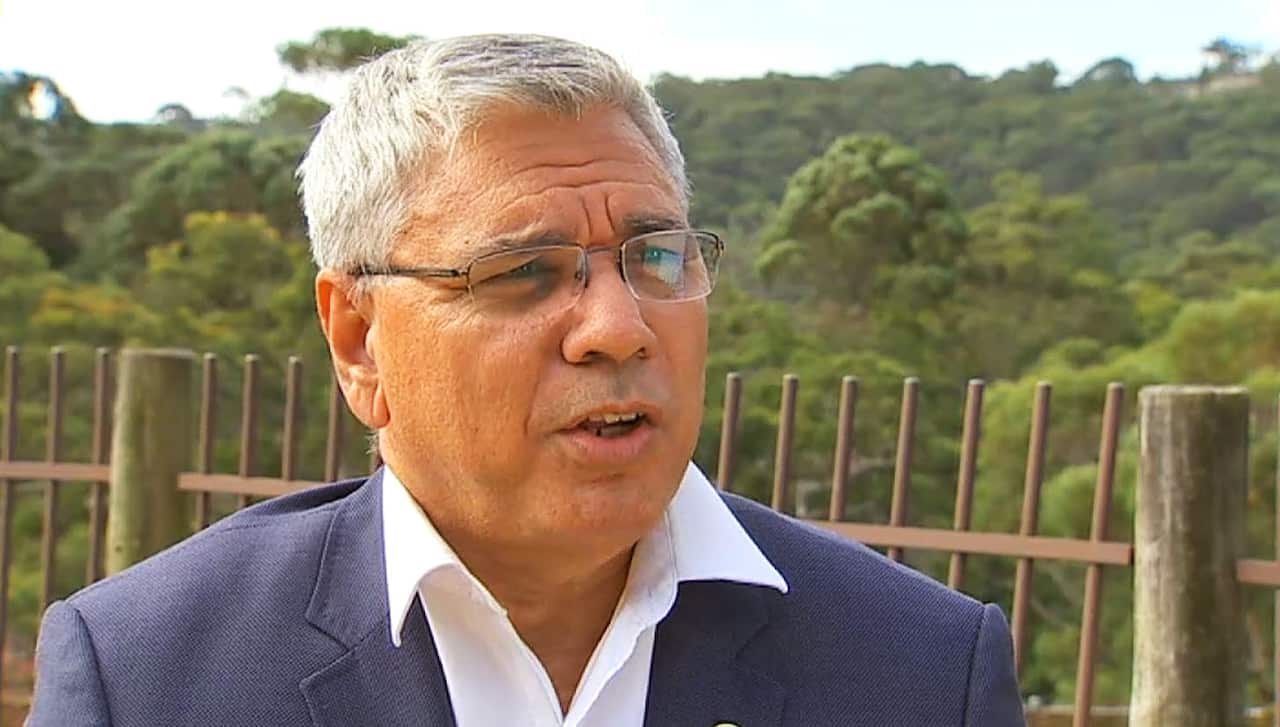 Man in glasses and suit with no tie outside.