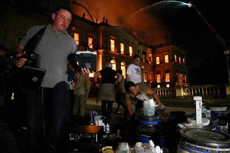 Employees recover objects from the National Museum of Rio de Janeiro, as a fire burns.