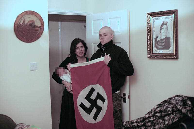 Adam Thomas and his partner Claudia Patatas with their new born baby in front of a Nazi flag. The couple named their child after Adolf Hitler.