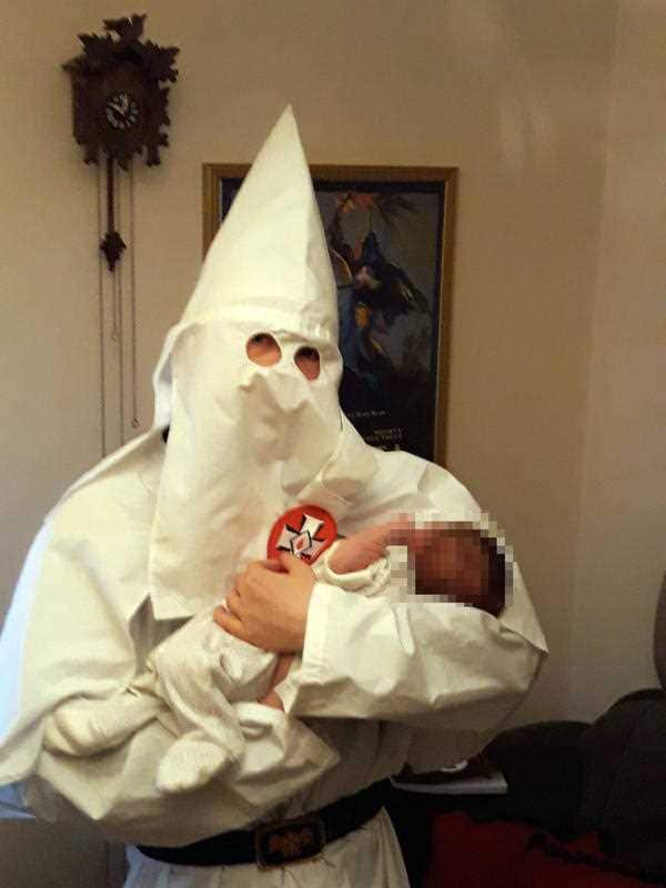 Thomas posing with his new-born baby, whilst wearing the hooded white robes of the Ku Klux Klan (KKK).
