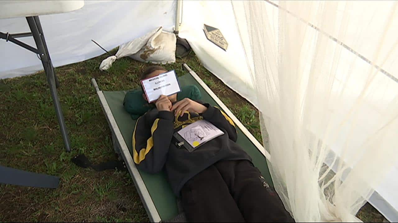 Student reads card about malnutrition and the symptoms many refugees suffer in camps. (SBS)