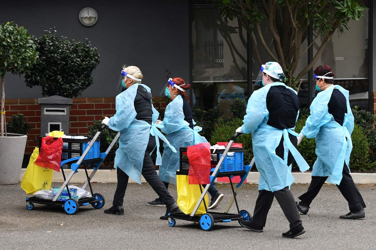 Healthcare workers wearing personal protective equipment and pushing small trolleys outside an aged care facility in Melbourne.