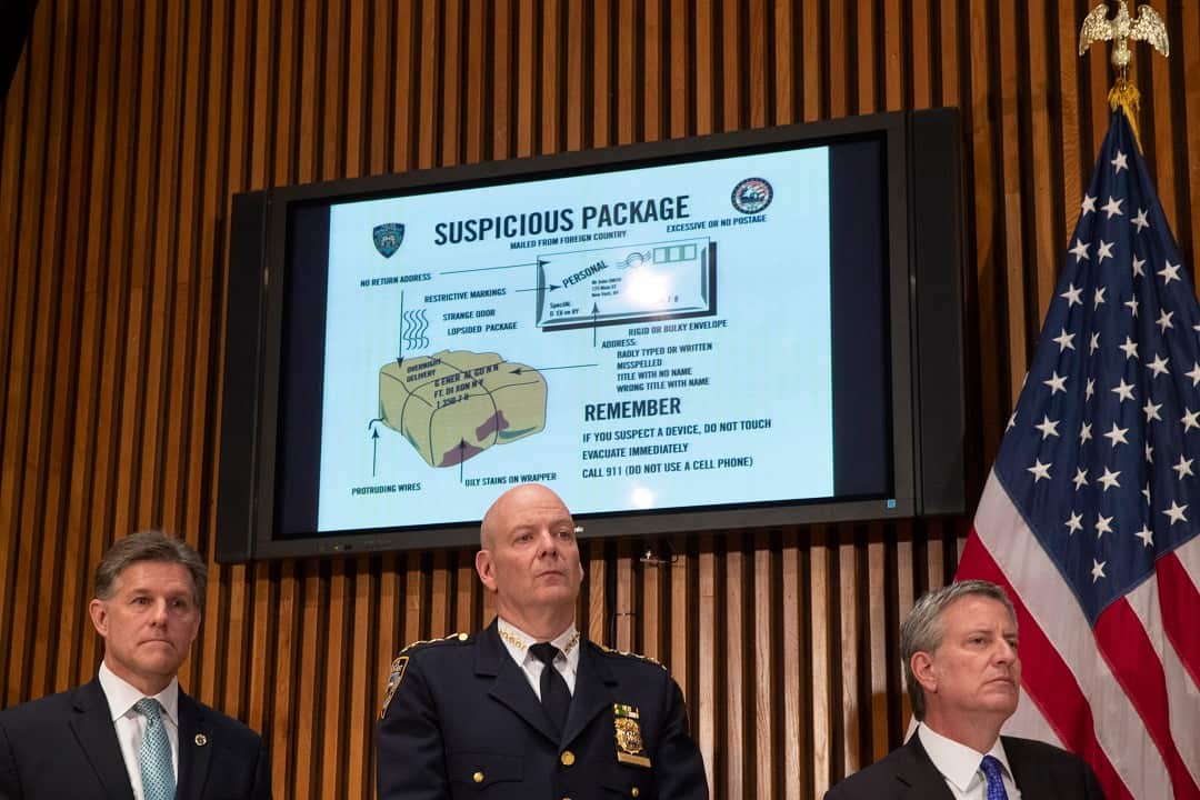 A monitor displays information about suspicious packages as NYPD Chief of Department Terence Monahan, centre, and NYC Mayor Bill de Blasio address the press.