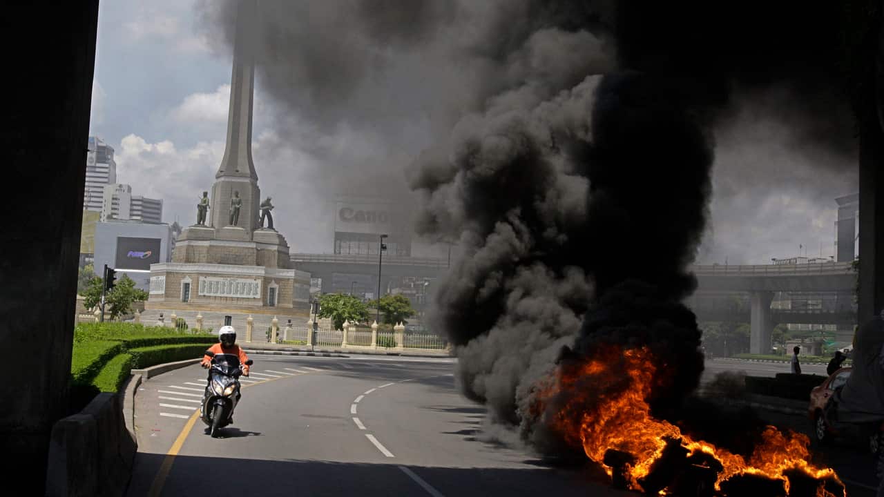 A motorbike drives past to thick smoke after anti-government protesters and supporters of ousted Prime Minister Thaksin Shinawatra set fires in protest.