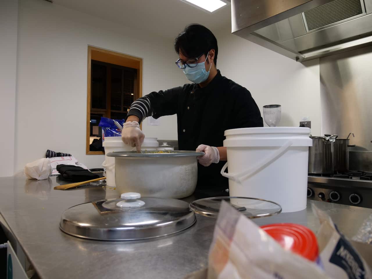 A young man wearing a mask stirring a big cooking pot