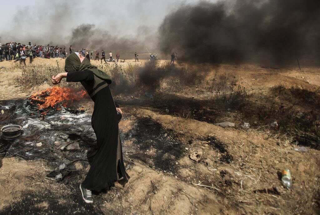 Palestinians throw rocks as they set tires on fire in response to Israel's intervention during a demonstration 'Flag Friday' within the 'Great March of Return' at Gaza-Israel border as the sky is covered with smoke after Palestinians set tires on fire in 