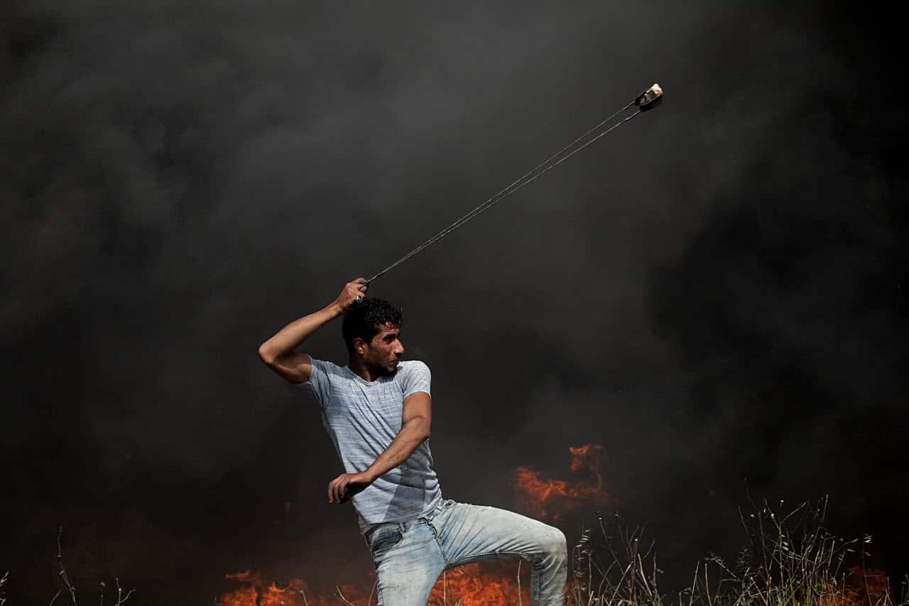 A Palestinian protester throws stones during clashes with Israeli troops near the border with Israel in the east of Gaza City, 13 April 2018