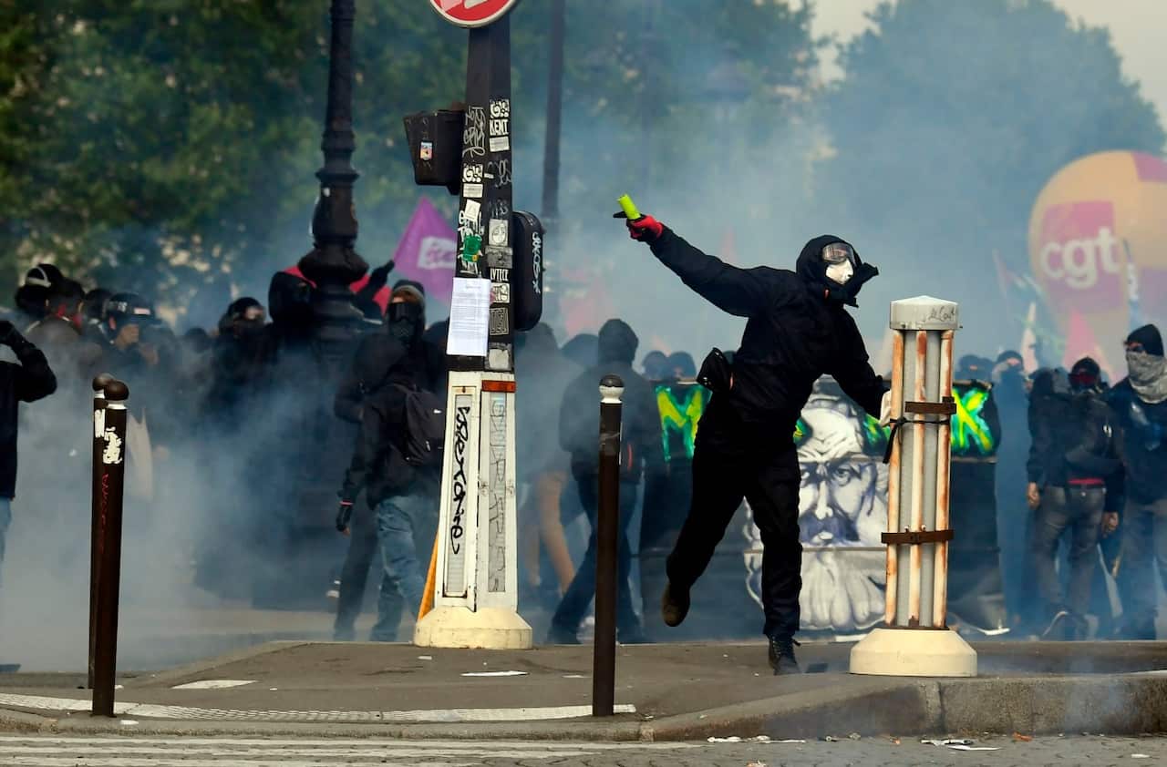 A protester throws a missile towards unseen police officials as teargas clouds rise during a demonstration on the sidelines of a march for the annual May Day wo
