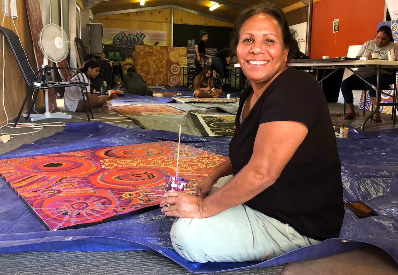 Artist Pearl Austen sits on the floor painting a canvass inspired by the Coober Pedy landscape.