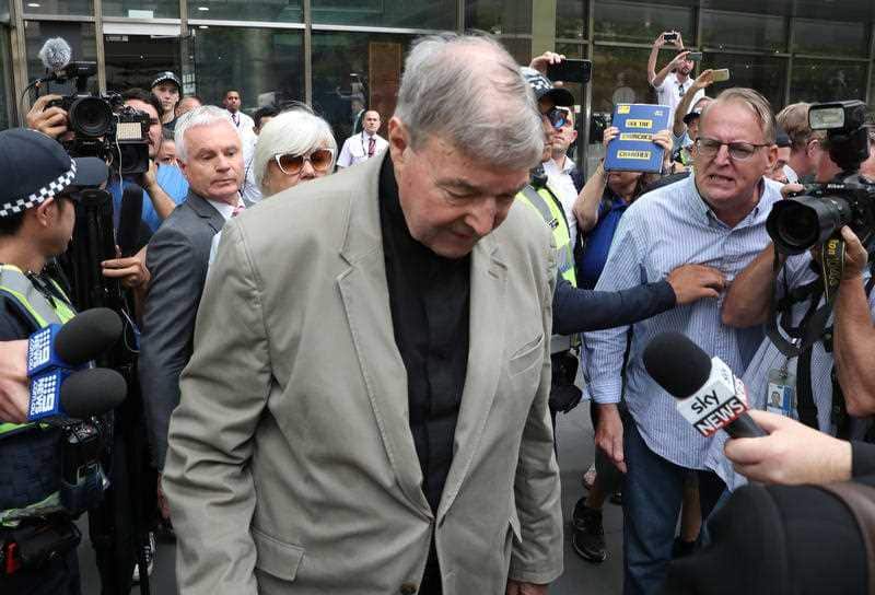 Pell pushes through the media pack outside court.