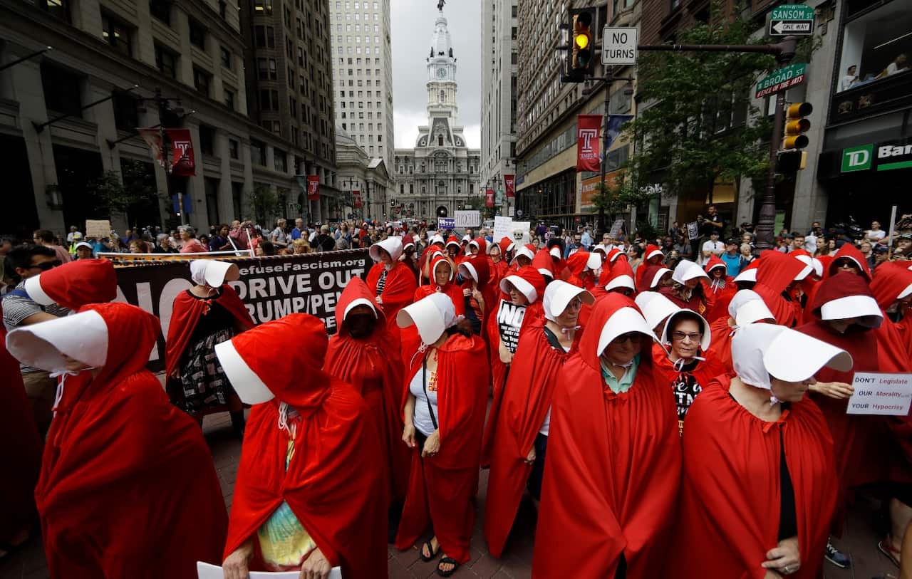 Protesters, in view of City Hall, center, dressed as characters from "The Handmaid's Tale," demonstrate against Vice President Mike Pence