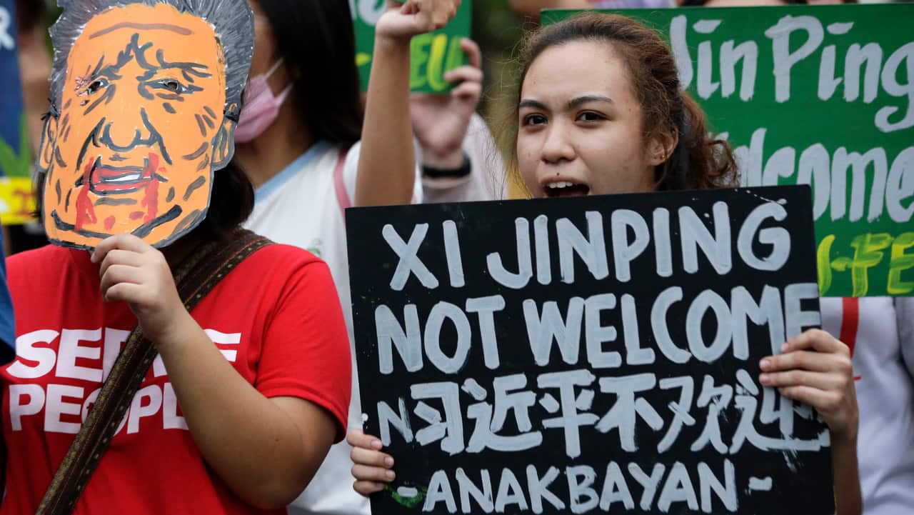 A student rallyist holds a slogan beside a mask with a face of Chinese President Xi Jinping as they protest against his visit.