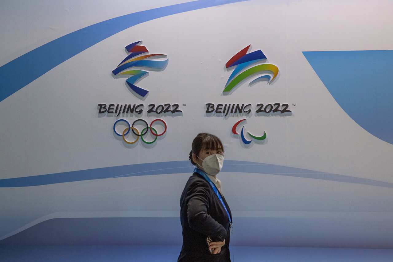A woman wearing a protective face mask walks past the logos of the Beijing 2022 Olympic and Paralympic Winter Games.