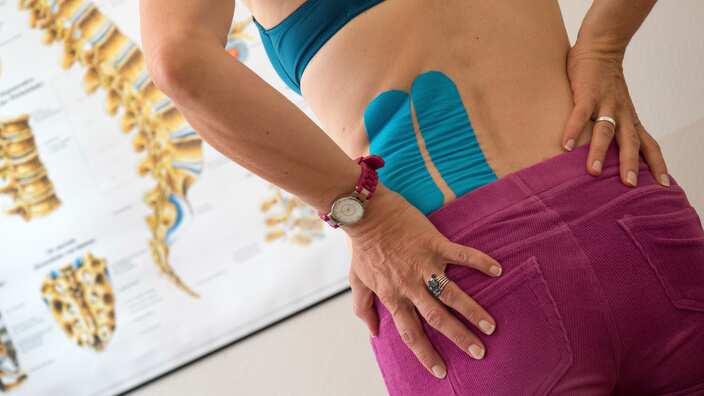 A woman with back pain looks at a diagram of a spine at a physiotherapist's office