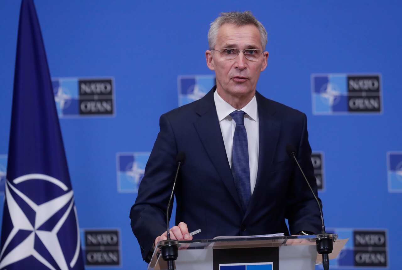 NATO Secretary General Jens Stoltenberg standing behind a lectern inside. The NATO flag is to his right.