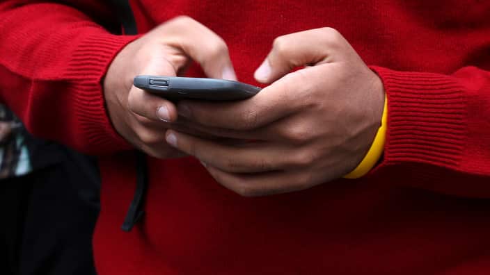 Two hands of a person wearing a red sweater hold a smartphone