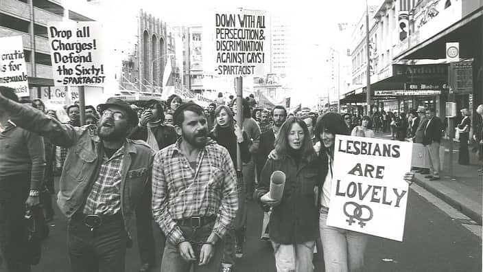 A balck and white photo of people marching and holding up signs with gay rights messages