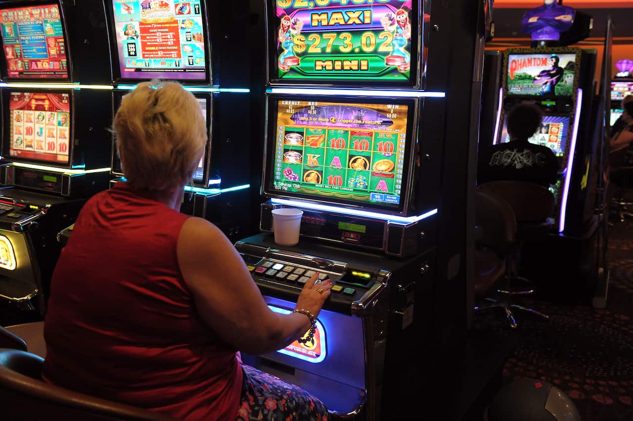 Woman sits at a pokie machine.