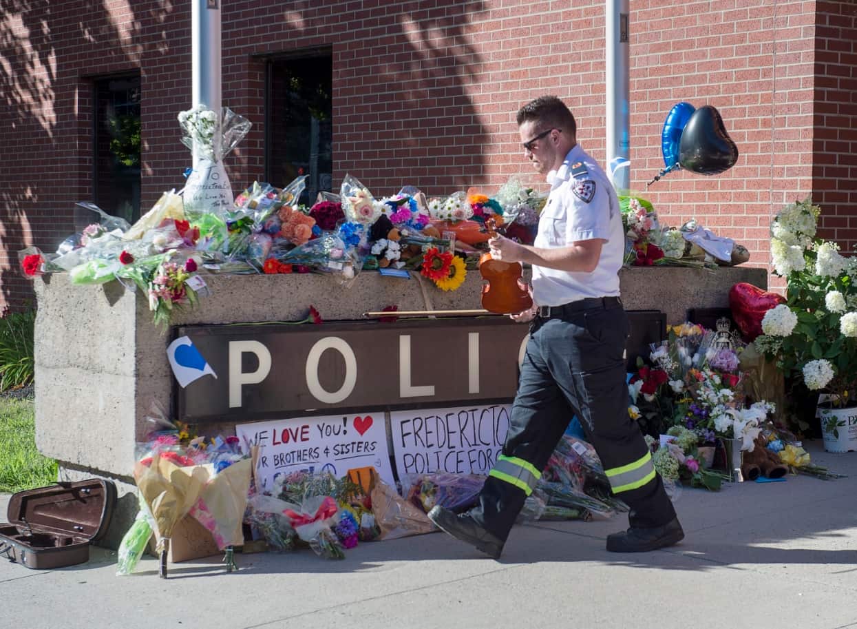 Paramedic Brian Fournier walks away after playing a hymn and placing a tribute at the police station in Fredericton, New Brunswick