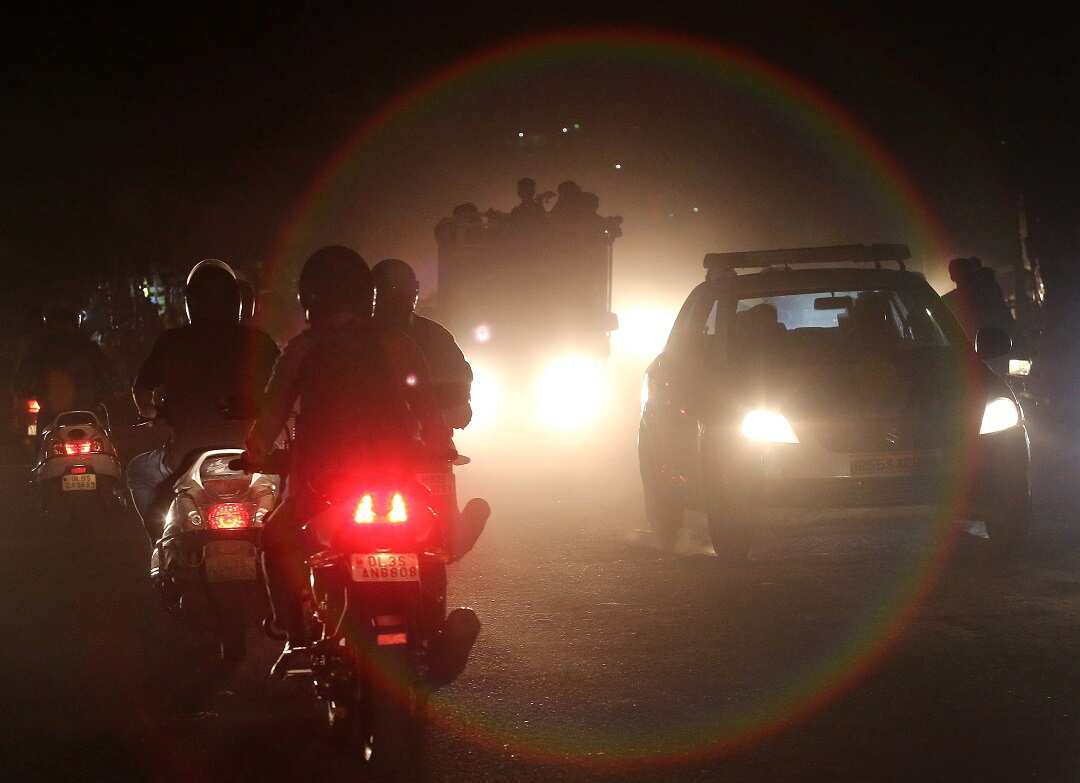 Indian people commute on motorcycles and cars through heavy dust and smog in New Delhi.