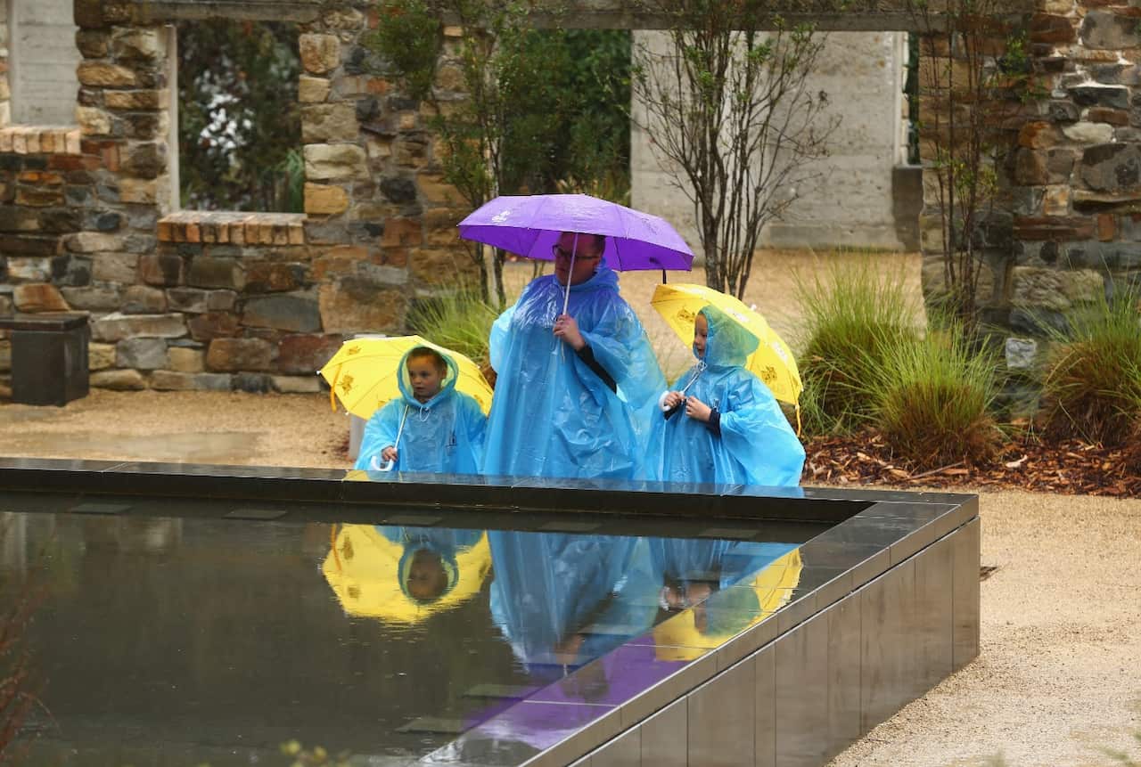 A family stands at the memorial pool, with the Broad Arrow cafe behind them during the 20th anniversary commemoration service