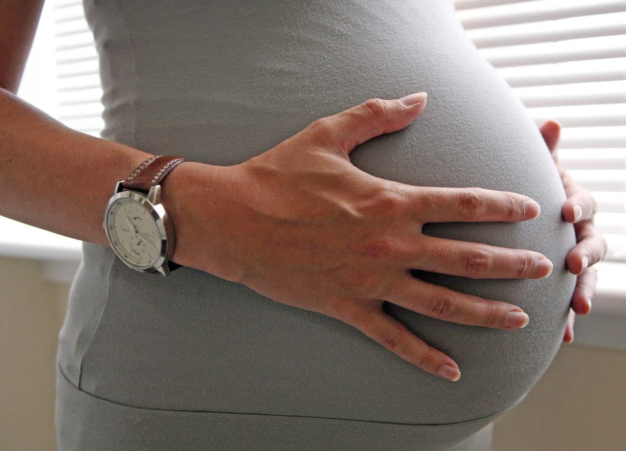 A woman holds her pregnant belly.