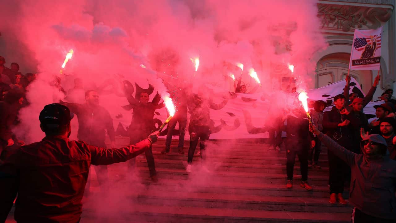 Tunisian protesters light flares and shout slogans.