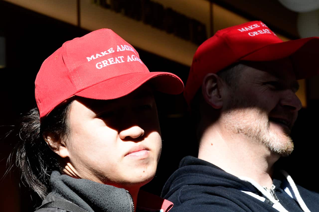 A pair of CPAC attendees watch on wearing “Make America Great Again” caps.