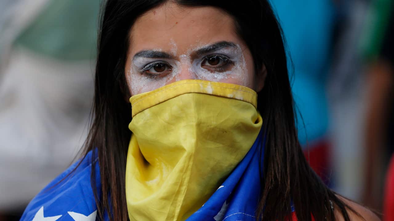 An anti-government protester covers her face with a Venezuelan flag, and uses toothpaste around her eyes to help lessen the effect of tear gas.
