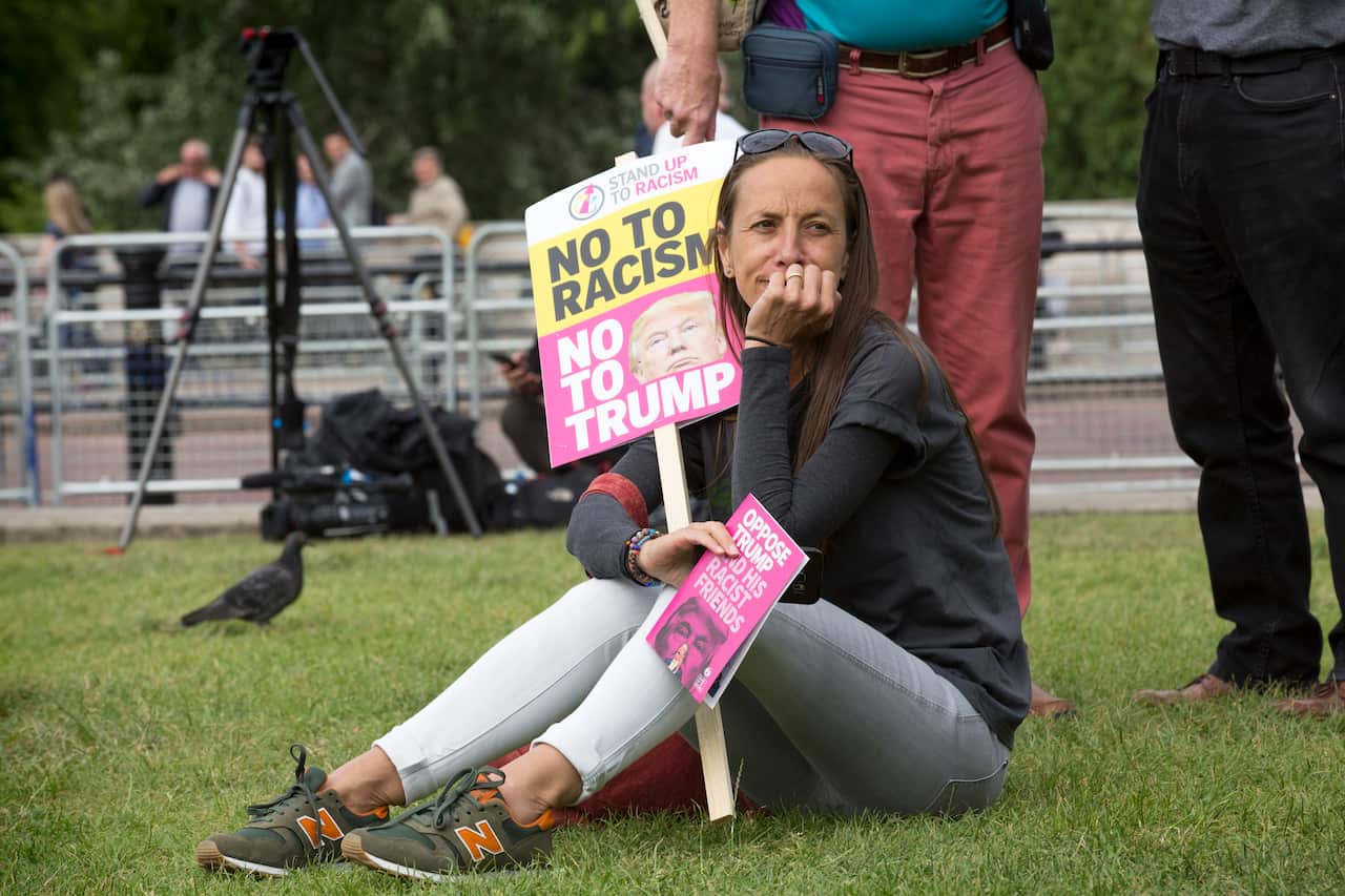 A woman sits with an anti-Trump placard during a protest against Donald Trump's visit to the UK.