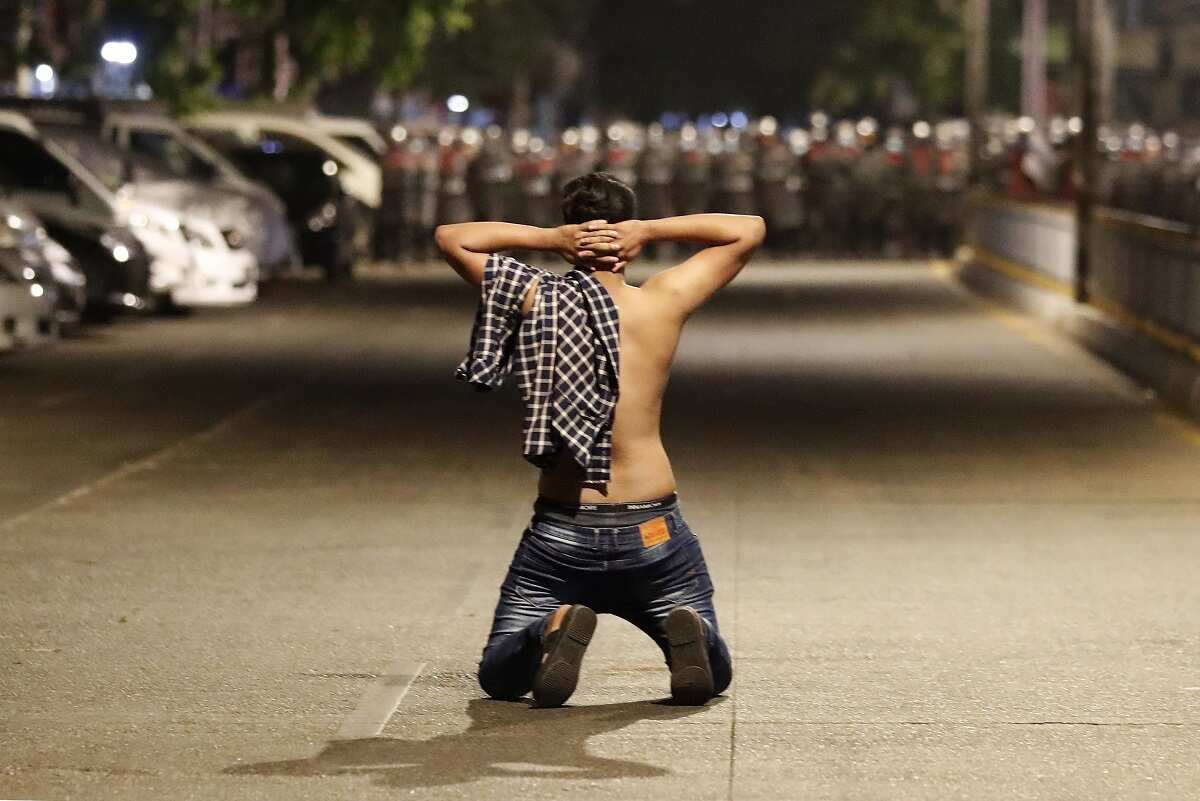 A demonstrator kneels as he protests against the military coup while riot police advance on a street as tensions rise in Yangon, Myanmar, 25 February 2021. 