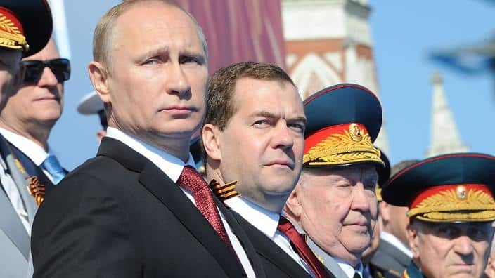 Vladimir Putin standing in a row of men, some in uniform.