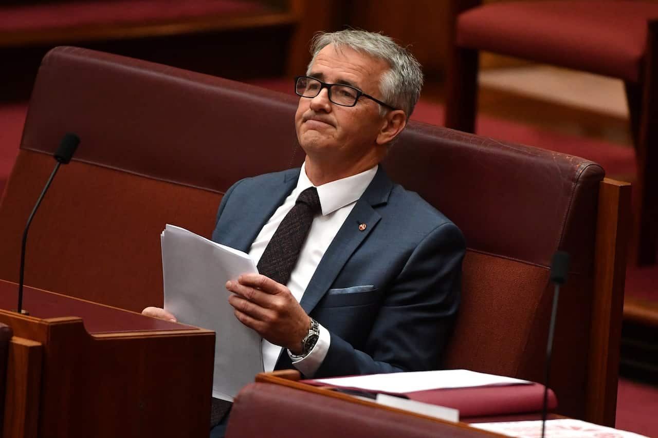 Liberal Senator Gerard Rennick sits back in his Senate seat holding a sheaf of paper. 