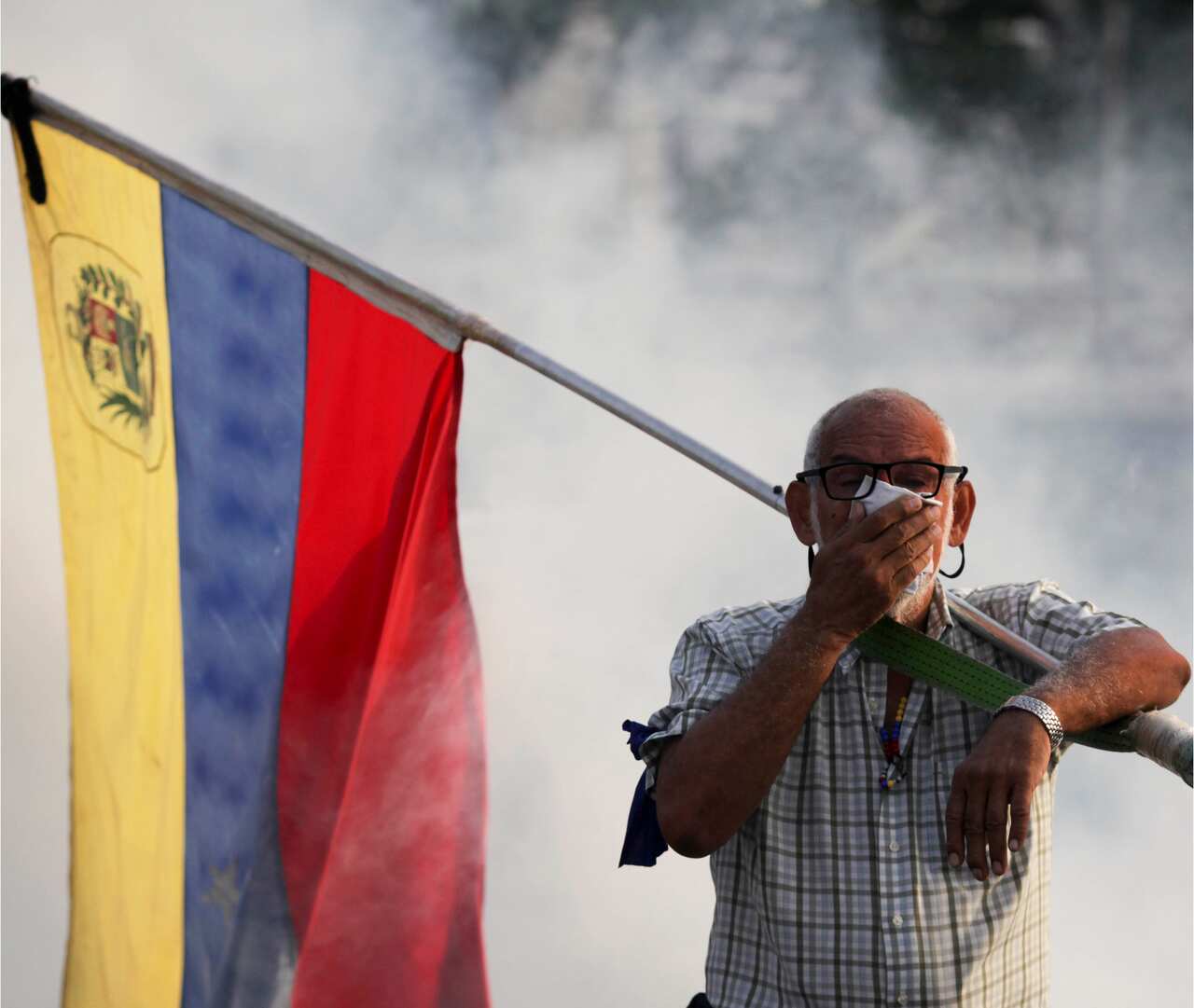 An opponent to Venezuelan President Nicolas Maduro carrying a Venezuelan flag covers his face amid tear gas fired by soldiers.