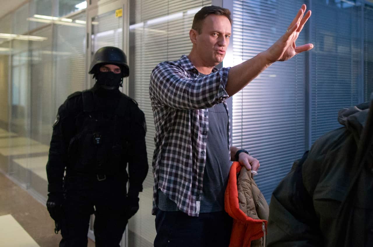Russian opposition leader Alexei Navalny speaks to the media, flanked by a police officer, following his arrest.