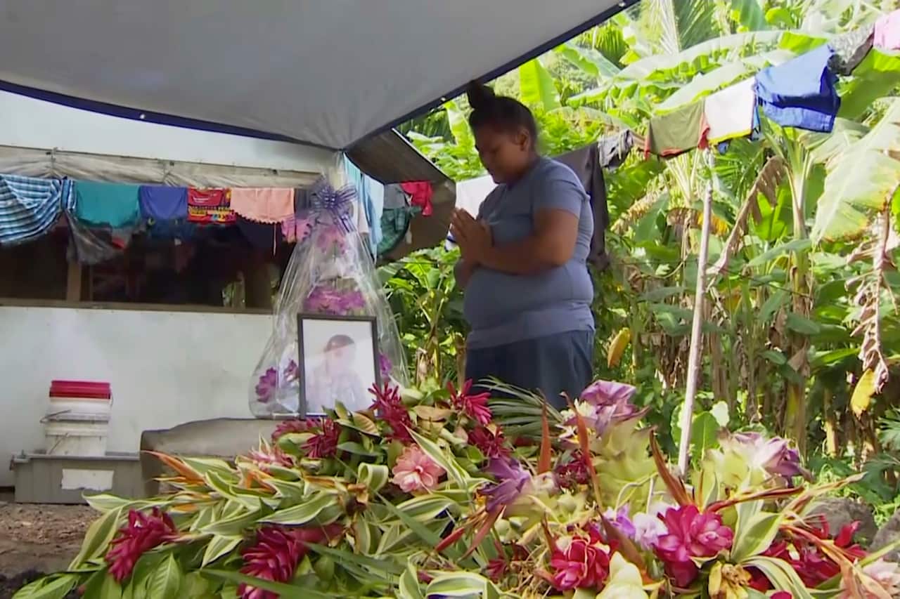 A Samoan woman prays in front of a portrait of her lost child, who died as a result of measles.