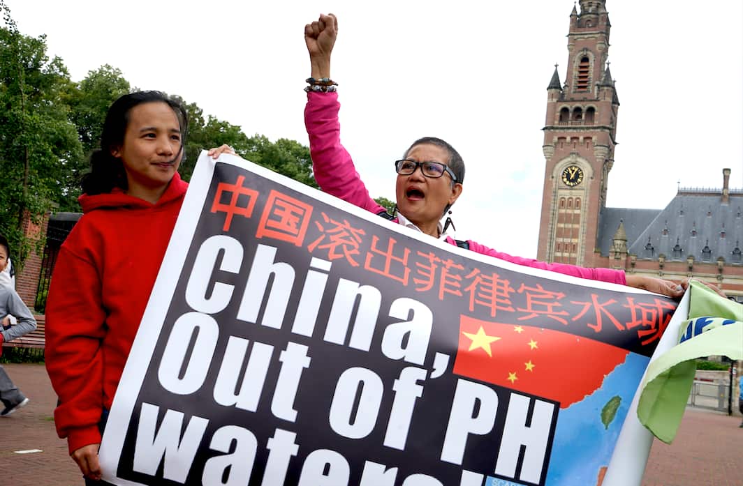protestors hold a sign reading 'China, Out of PH waters. 