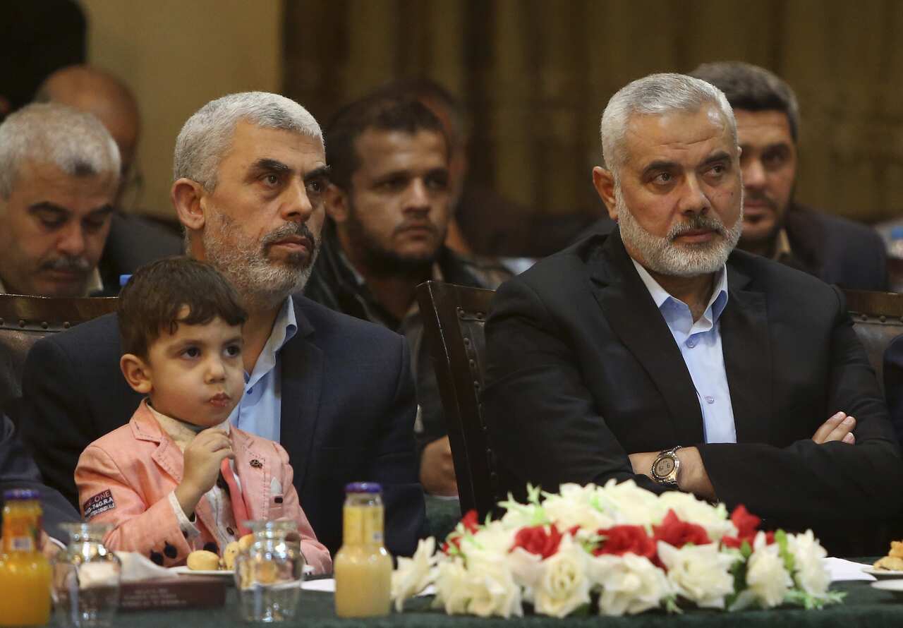 Yahya Sinwar, a middle-aged man with short grey hair, holds a young boy on his lap. Sitting next to him is another top Hamas leader, Ismail Haniyeh, who also has short grey hair and is wearing a suit.