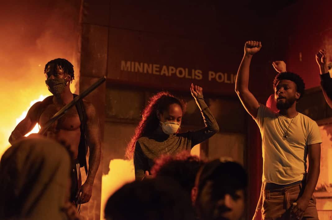 Protestors stand, fists raised, in front of the burning Minneapolis 3rd police precinct.