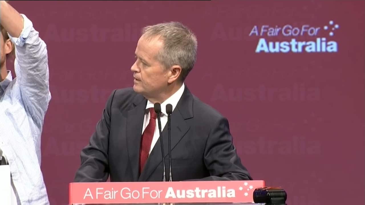 A bemused looking Mr Shorten watches as the protesters take the stage.