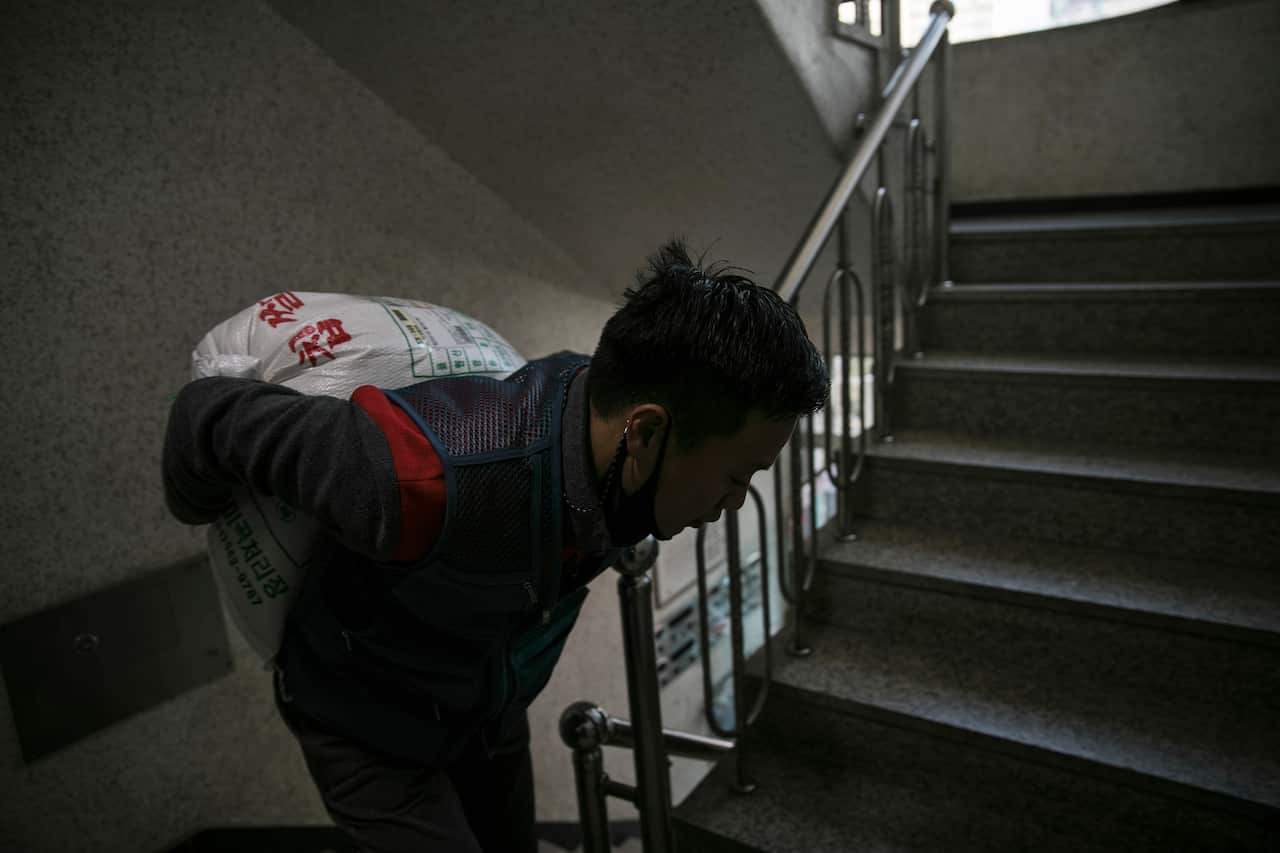 Park Ki-Ryeon hauls a bag of rice up flights of stairs for a customer in Seongnam, South Korea, 30 November, 2020. 