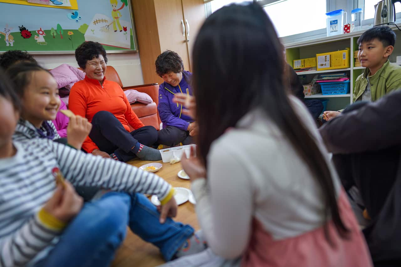 Hwang Wol-geum, 70, left, and Kim Mae-ye, 64, share snacks with students at Daegu Elementary, in Gangjin County, South Korea.